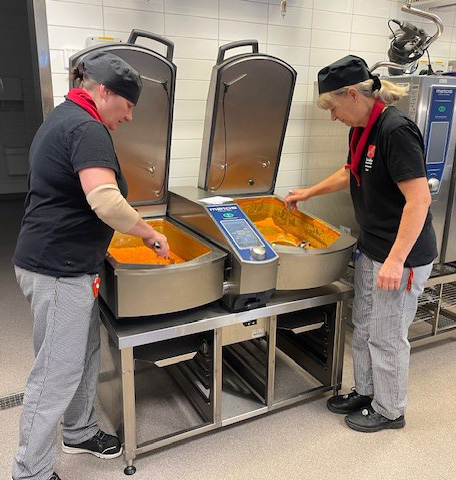 Måltidspersonal rör i stora grytor