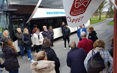 Människor står utanför bussen och lyssnar på en kvinna som pratar.