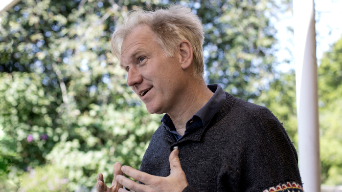 Göran Christiansson har en stickad tröja och blont hår. Han står under ett nötträd 