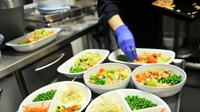 Personal lägger  upp portioner på tallrikar. På bilden syns en hand som fördelar ärtor och andra grönsaker.