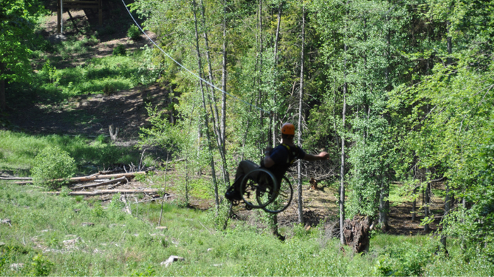 Man i rullstol åker zip-line mellan träden.