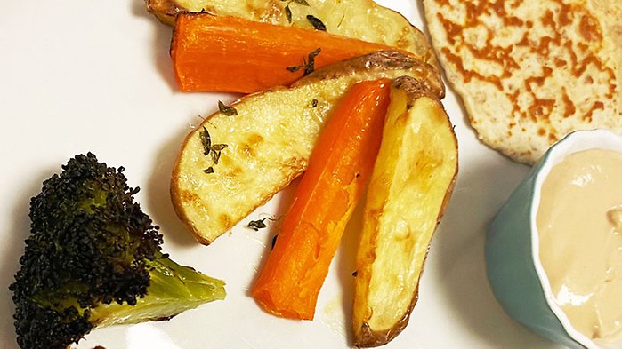 Ugnsbakade grönsaker och rotfrukter på ett fat. Broccolibukett och potatis- och morotsklyftor. 