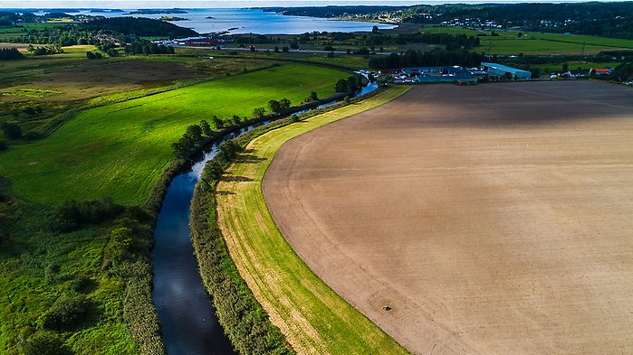 Flygbild. Å som rinner genom svenskt jordbrukslandskap.