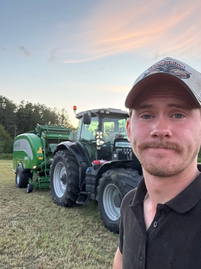 Linus Olsson vid sin traktor. Han har keps på sig.