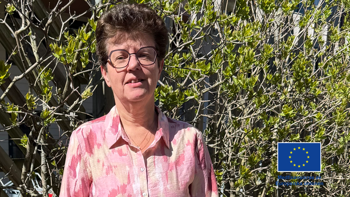 Irene Oskarsson har ljus blommig blus, mörkt hår och står utomhus i grönska 
