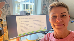 Jennie Cederholm Björklund tar en selfie framför en dataskärm som visar en presentation med rubriken "Communities of Practices". Bakgrunden visar ett ljust kontorsrum med fönster som leder till ett uterum.