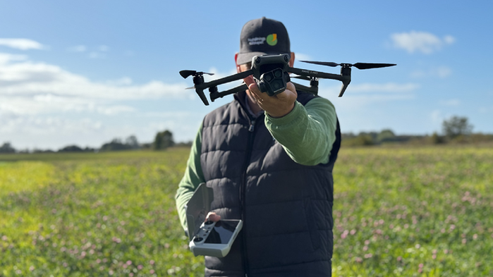 En man håller en drönare och kontroll ute på ett fält