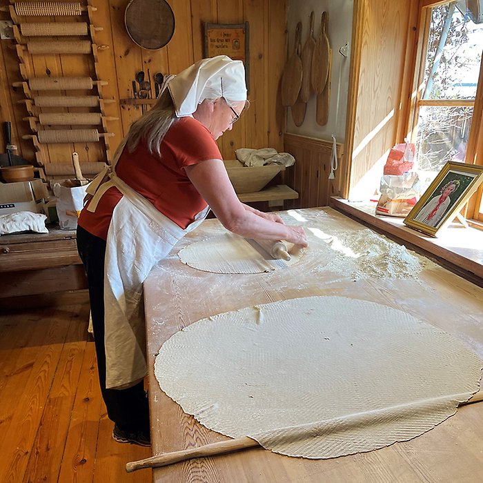 Kvinna i förkläde och huckle vid bakbord.