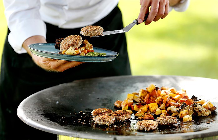 En kock arbetar vid en stekhäll. Händerna syns och rätterna som lagas är gjorda på odlade proteiner