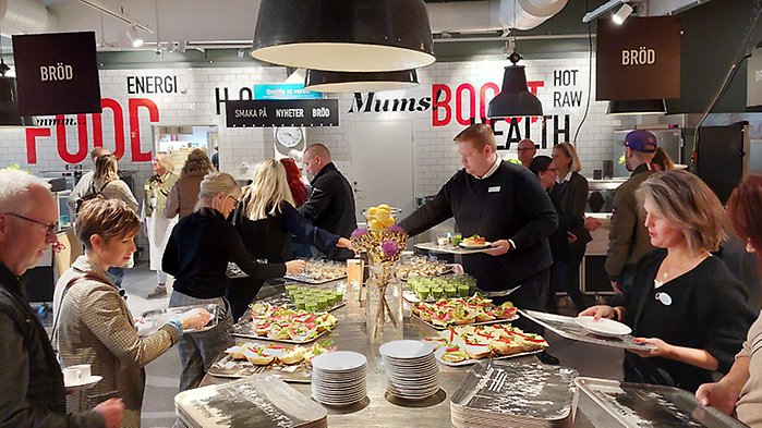 Skolmatsal. Flera vuxna personer tar frukost vid buffébord.